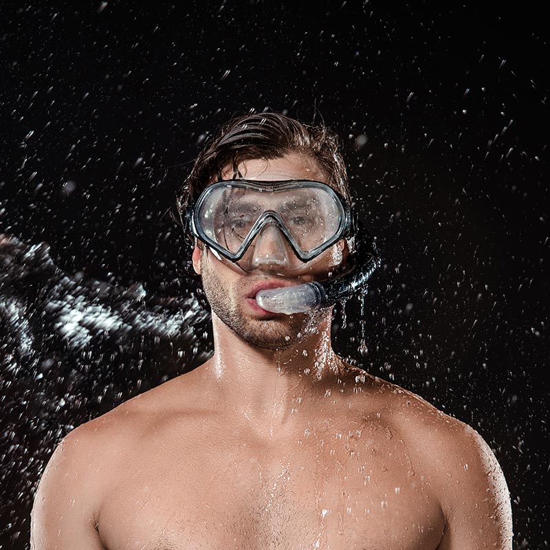 Mann mit Tauchmaske wird von Wasser nass gespritzt